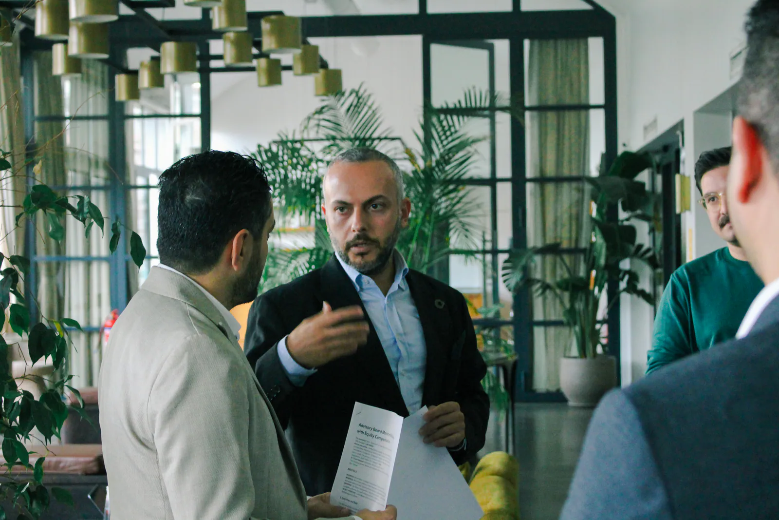 A mentor holding notes and speaking in a space surrounded by plants