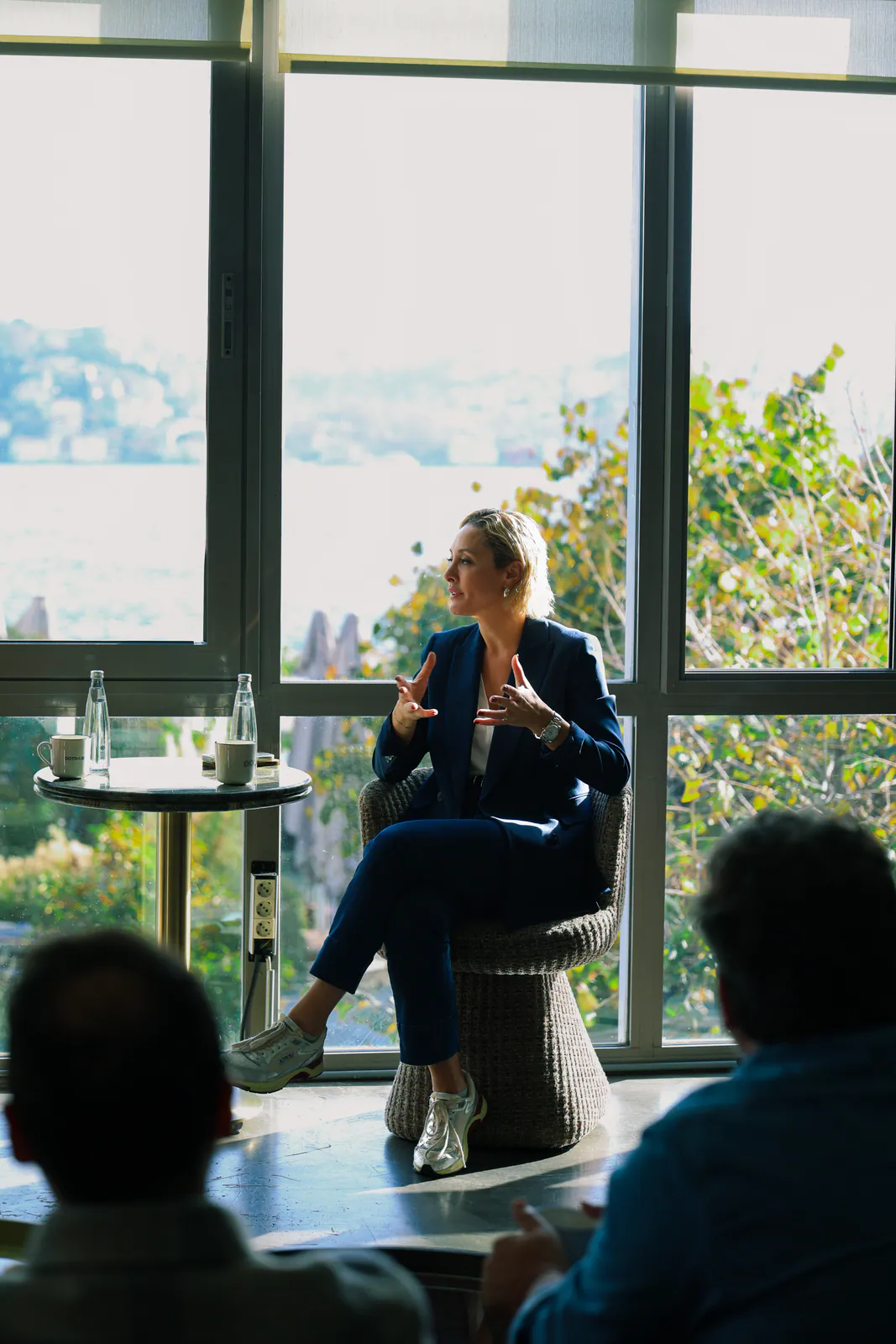 Boğaz manzaralı pencerenin önünde konuşan bir kadın ve onu dinleyen üyeler